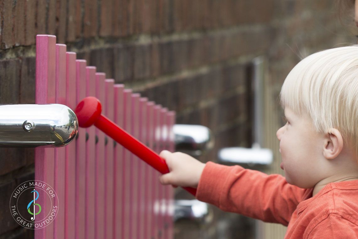 close up of blonde baby hitting pink wall mounted xylophone with a red beater