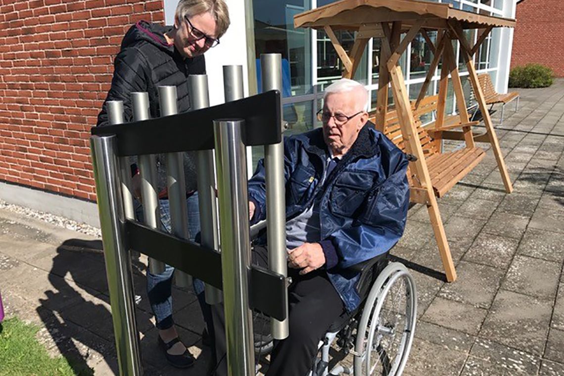 older man in a wheelchair playing an outdoor musical instrument in care home garden