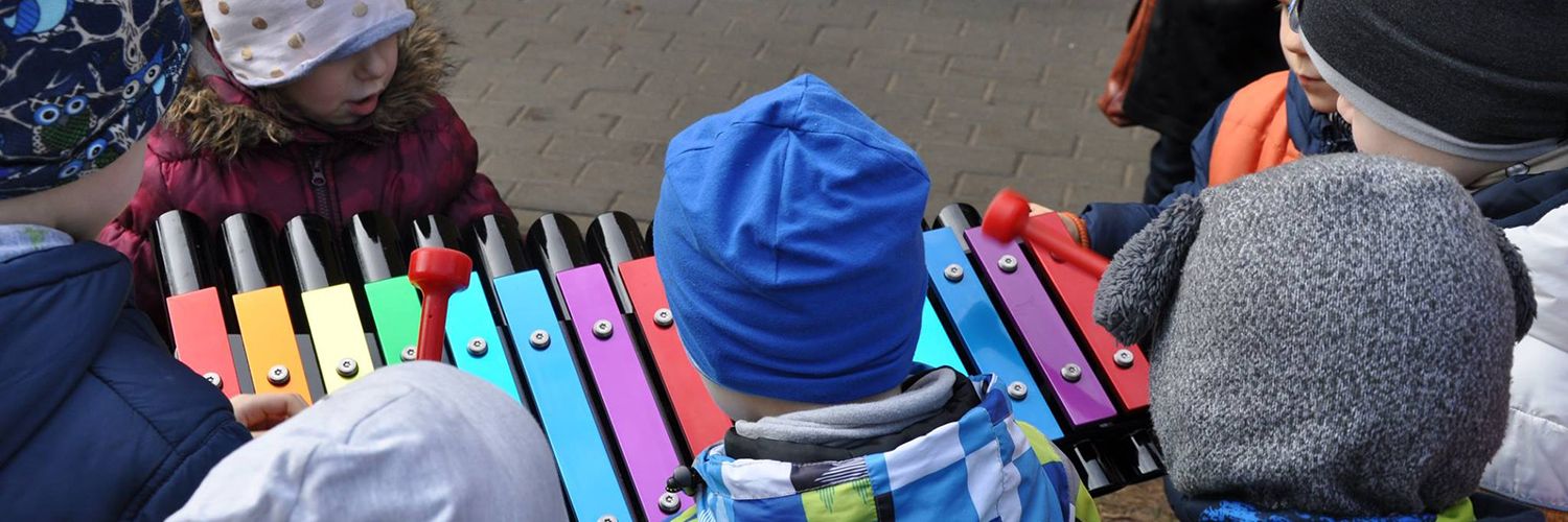 lots of little children in woolly hats surrounding a colourful outdoor xylophone in a playground