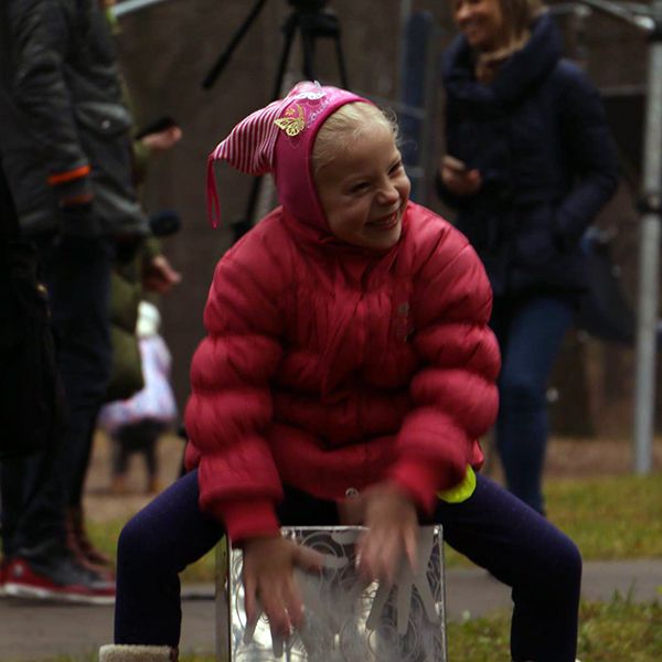 Little girl in bobble hat sat on a stainless steel cajon drum in a city park