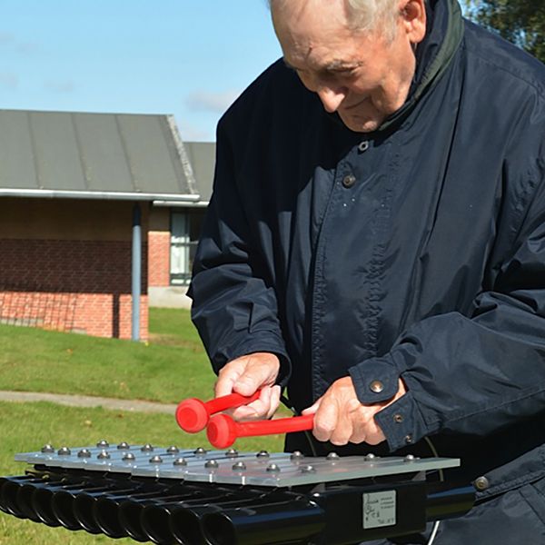 Older man playing an outdoor xylophone in care gome garden