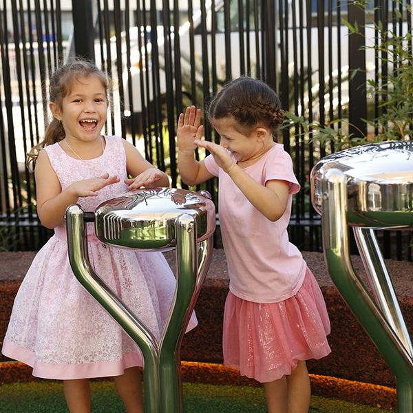 two little girls playing stainless steel tongue drums in shopping precinct playground