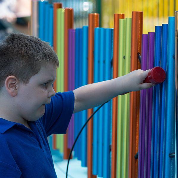 boy with special needs playing rainbow coloured chimes outdoors