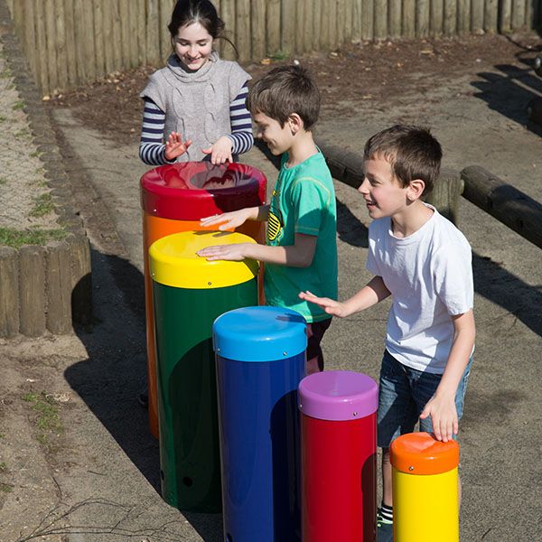 three children playing on a set of five rainbow coloured drums in a playground
