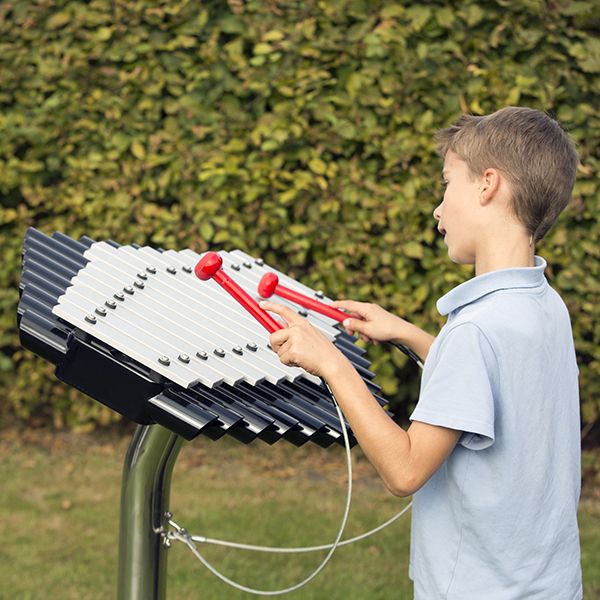 Schoolboy playing  a silver outdoor xylophone in a playground