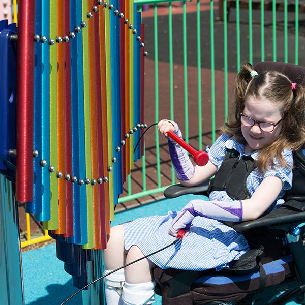 young boy with special needs playing colourful musical chimes in the playground