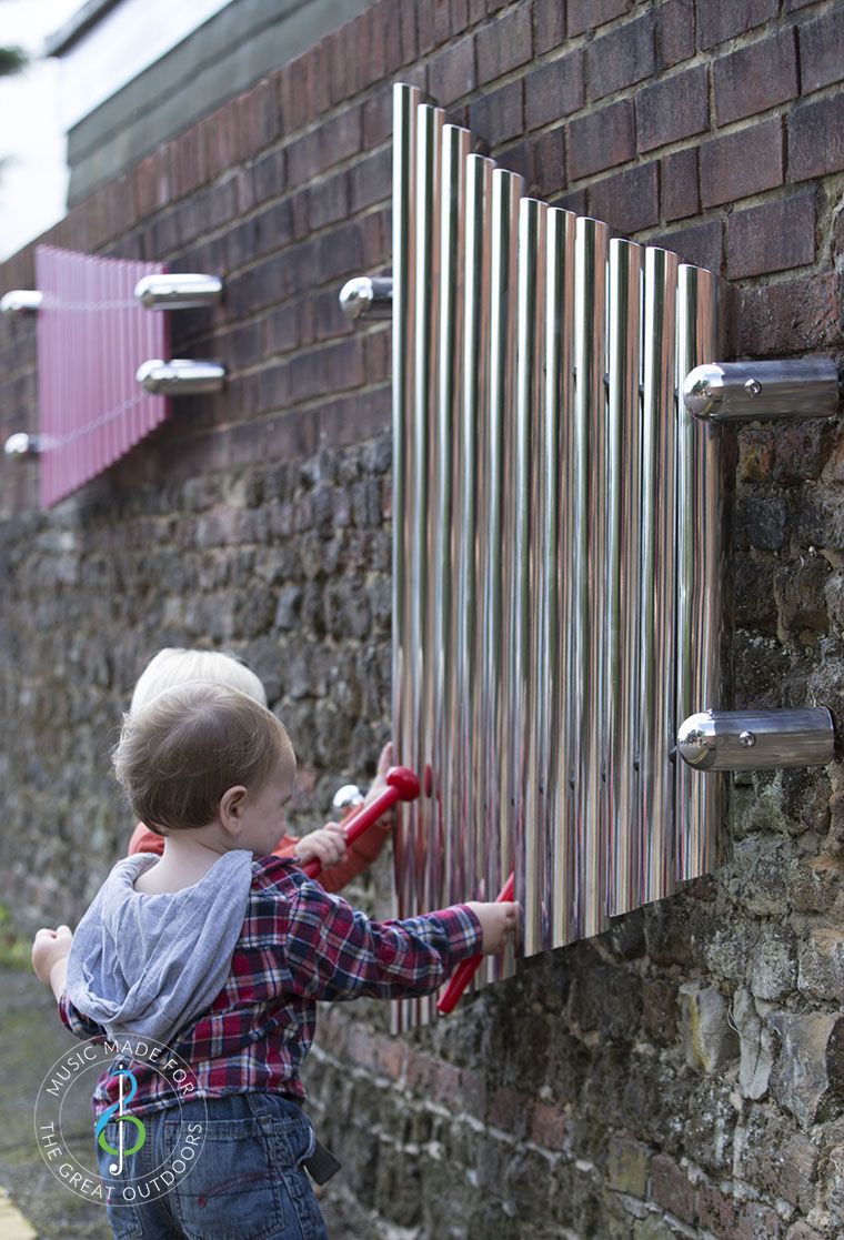 two toddlers stood playing large mirrored wall chimes with red beaters