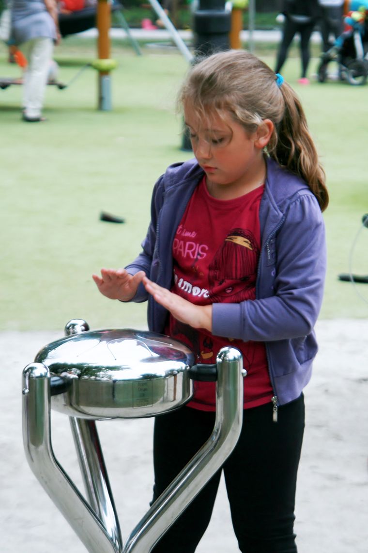 Young girl playing a silver steel tongue drum in a playground