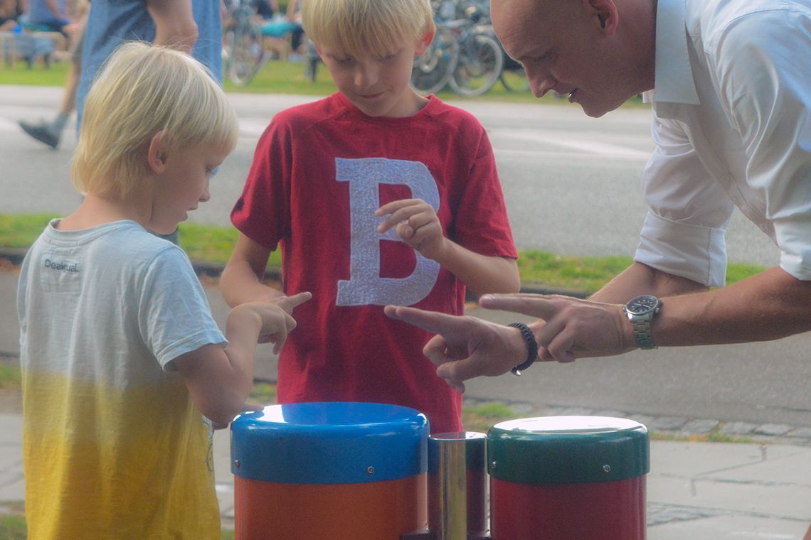 man with two boys plying conga drums in a playground