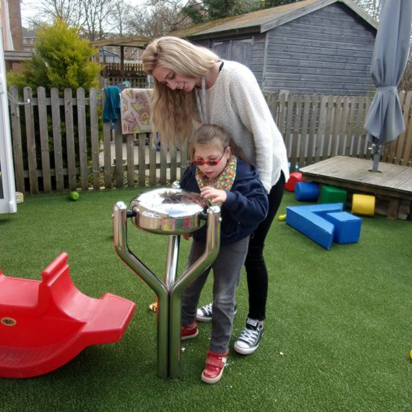young girl and her carer playing a stainless steel outdoor tongue drum together in special needs school playground