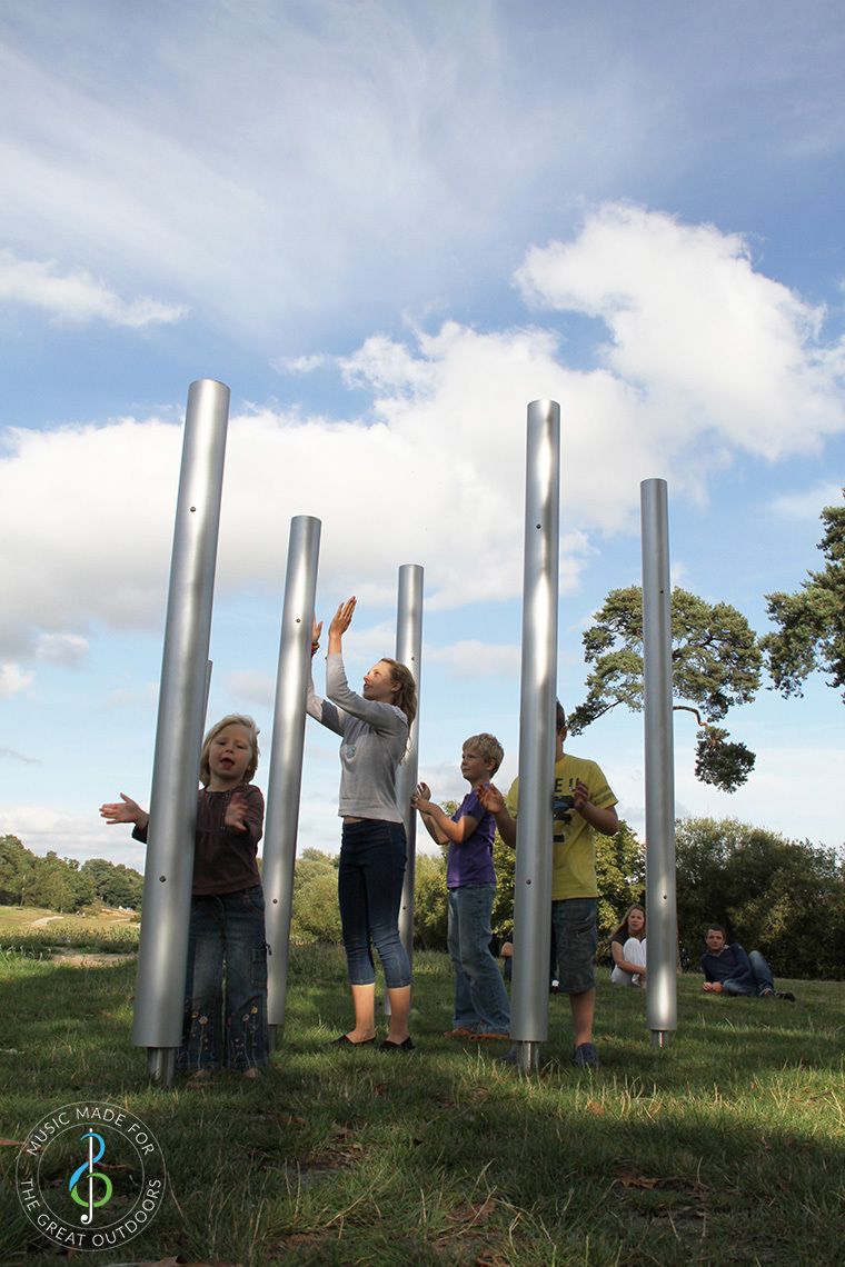 Family playing on five large outdoor chimes together in the park