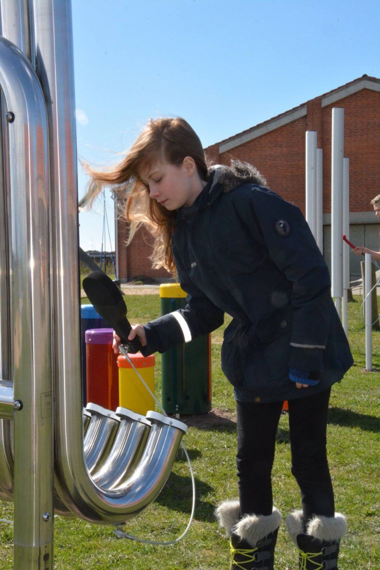 Girl hitting pipes of a large Aerophones with a black paddle in a School Playground