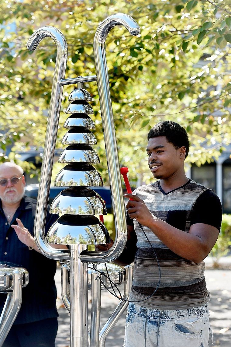 Black man playing a tall silver bell tree in the park