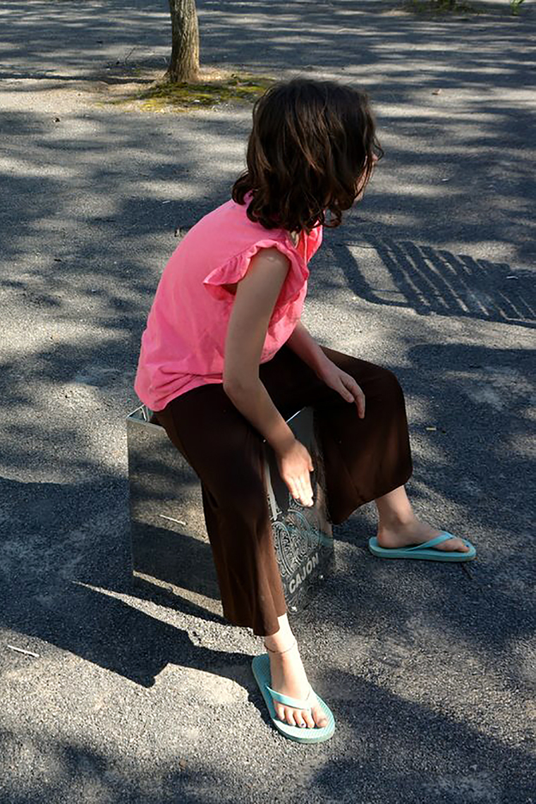 a young girl sitting on a metal outdoor cajon drum designed for musical parks and playgrounds