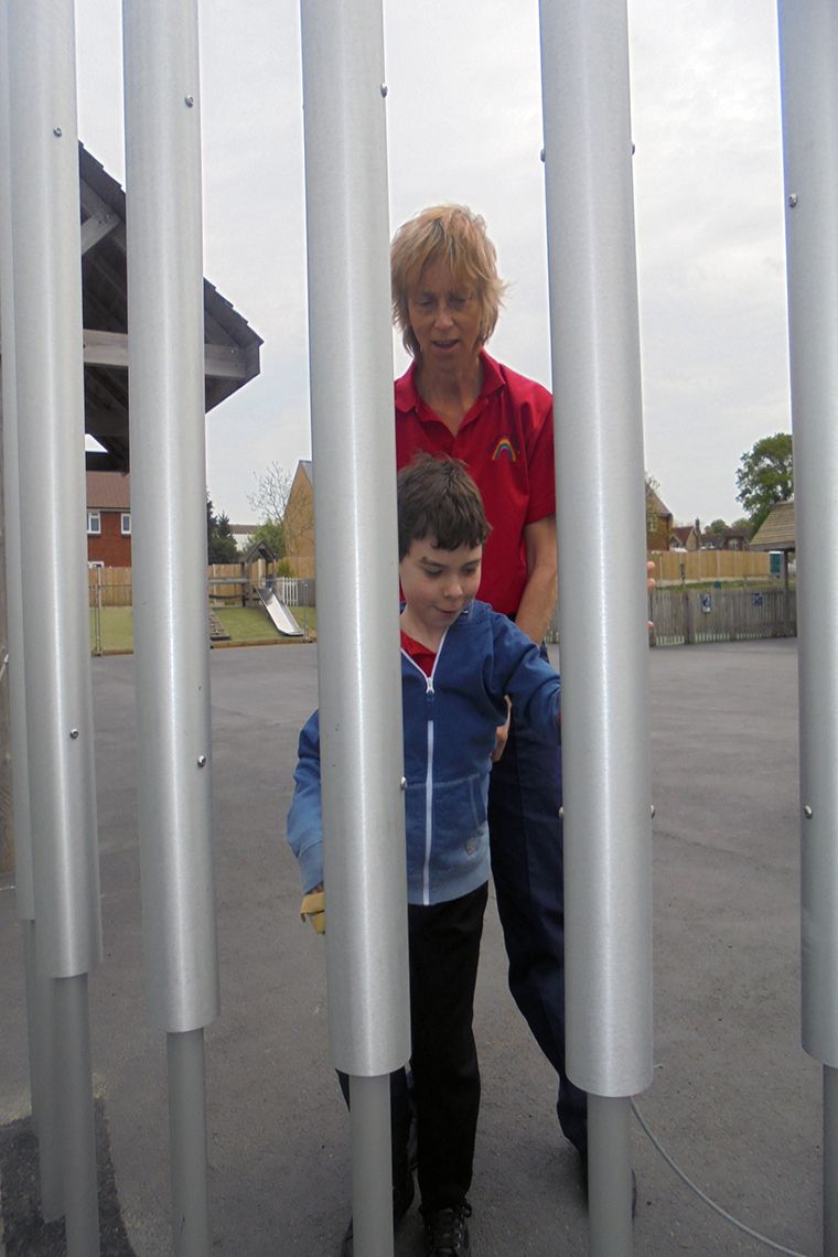 boys with special needs being encouraged to play large playground chimes by his carer
