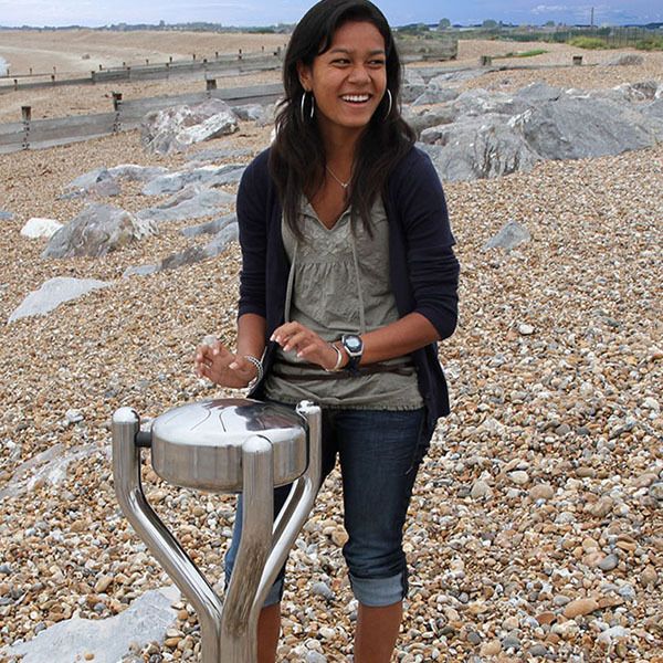 Girl on a beach playing a stainless steel tongue drum mounted on a stand