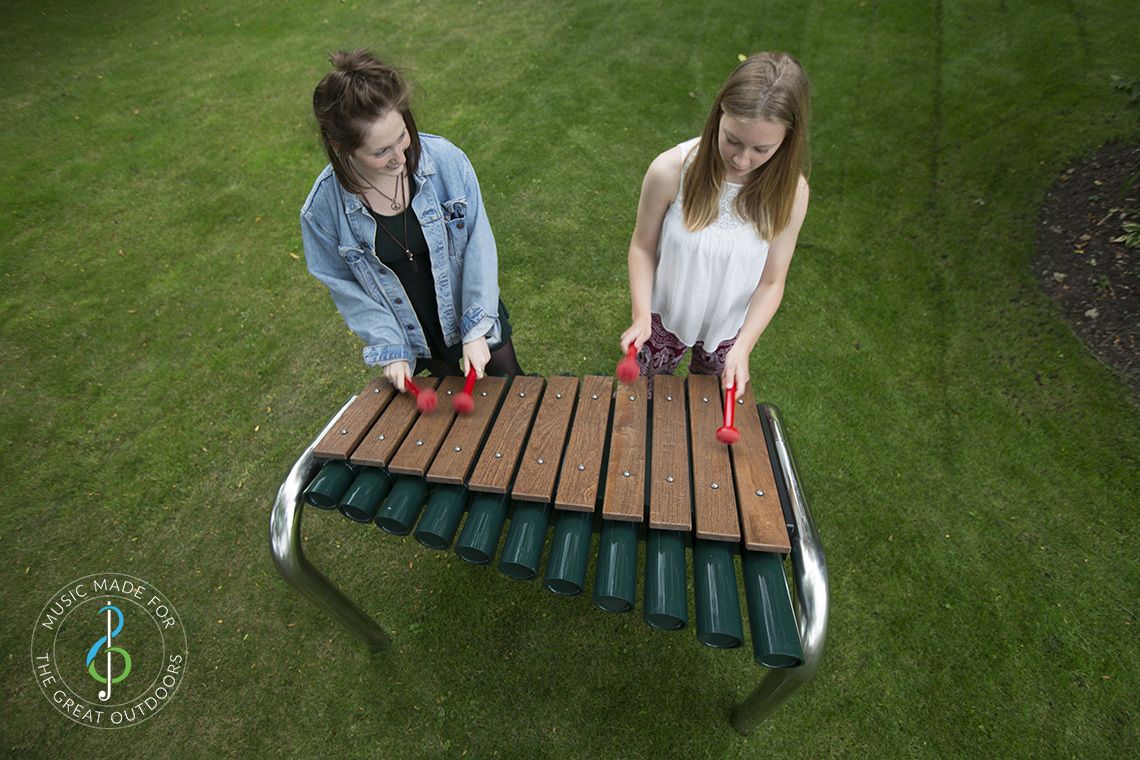looking down on two teenage girls playing large outdoor marimba with wooden notes in park