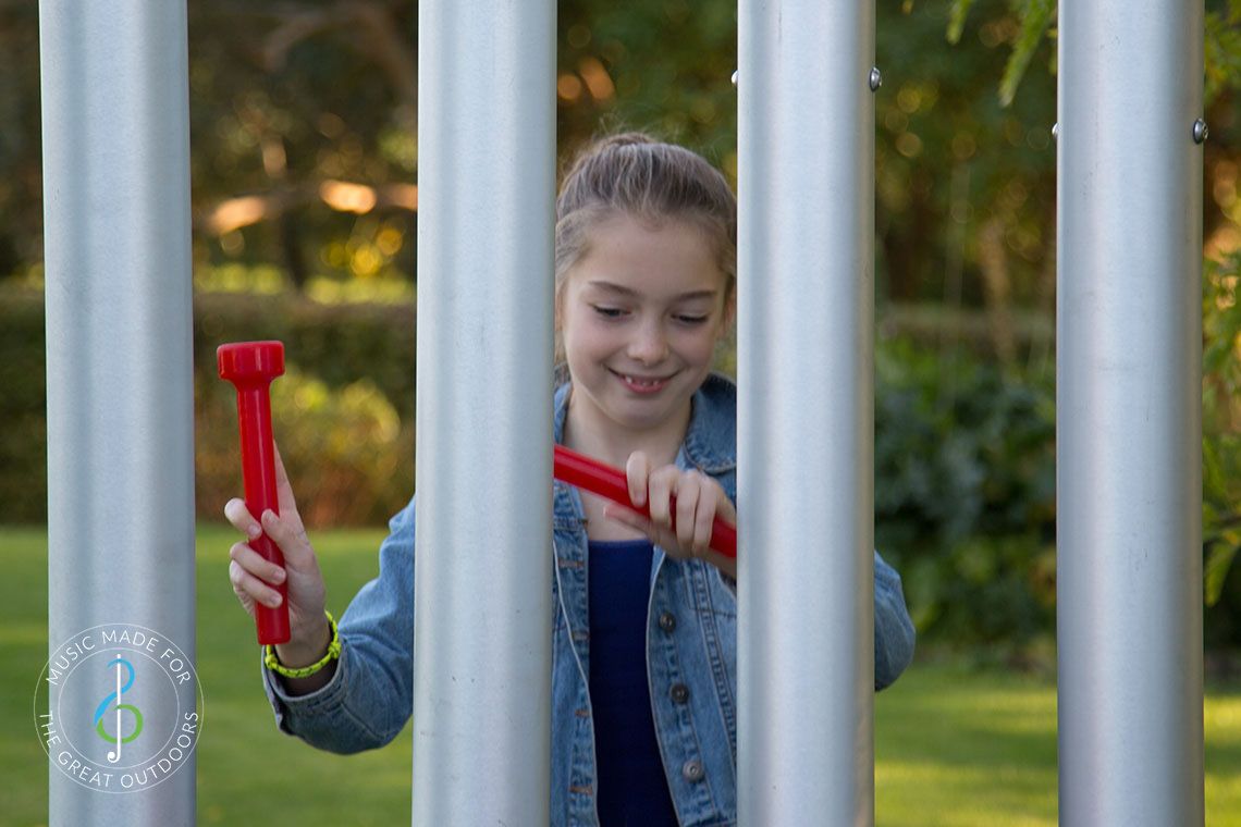 Teenage Girl hitting large outdoor chimes with red beaters in playground