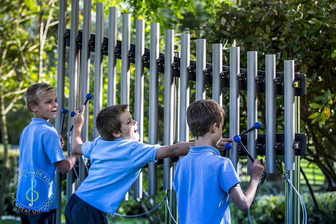 three schoolboys in blue uniform playing on outdoor musical chimes in playground