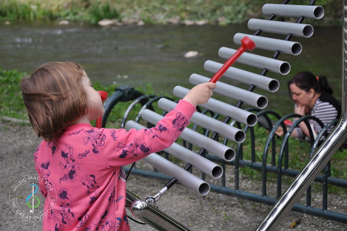 small girl playing large xylophone in a park