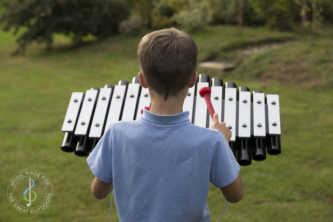 back of boy playing outdoor xylophone with silver notes and black resonators