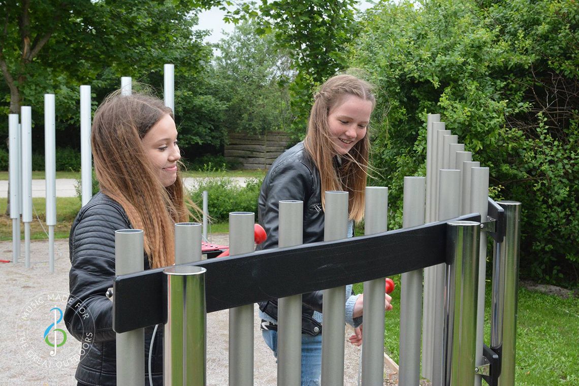 teenage girls in music park playing on outdoor musical chimes