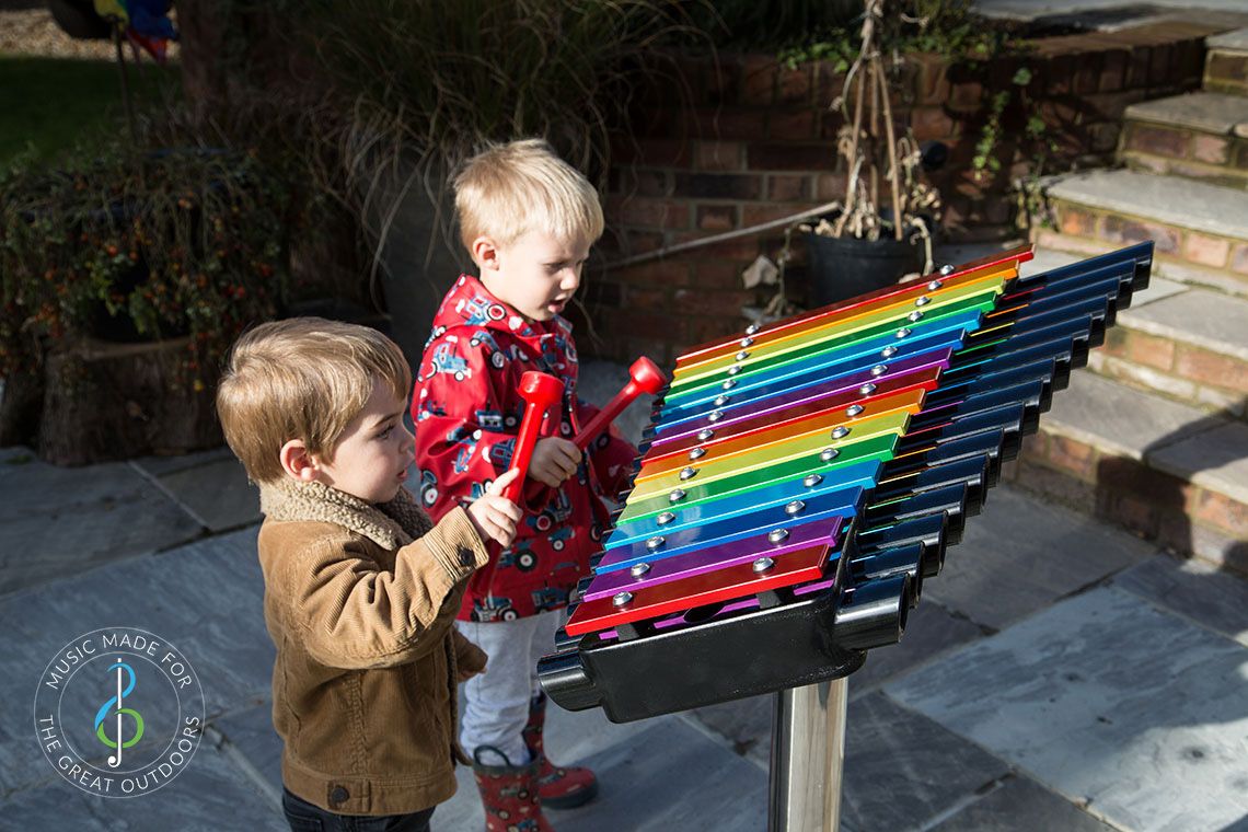 Two Young boys Playing Rainbow Coloured Xylophone Outdoors