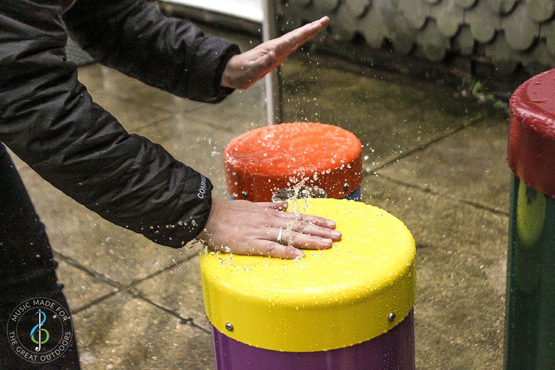 Pair of hands slapping down on bright coloured outdoor congas drums in the rain
