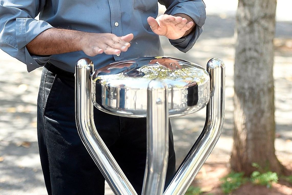 pair of male hands playing a stainless steel tongue drum