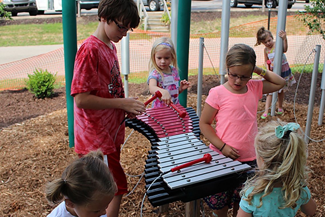 Group of children in a playground laughing and playing a large outdoor xylophone