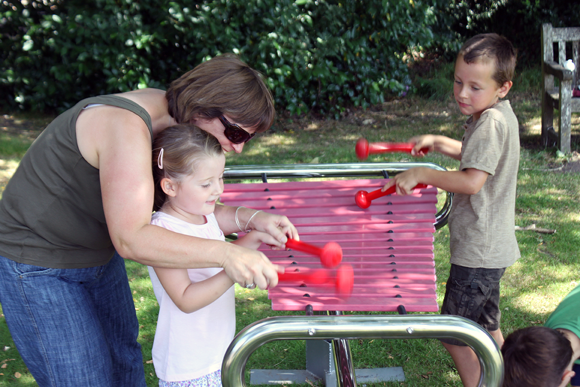 two children and mother playing a large marimba with pink notes in the park