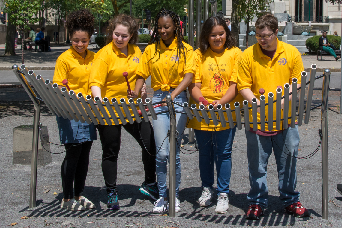 Five Teenagers dressed in yellow t-shirts playing an outdoor musical instrument in Syracuse USA