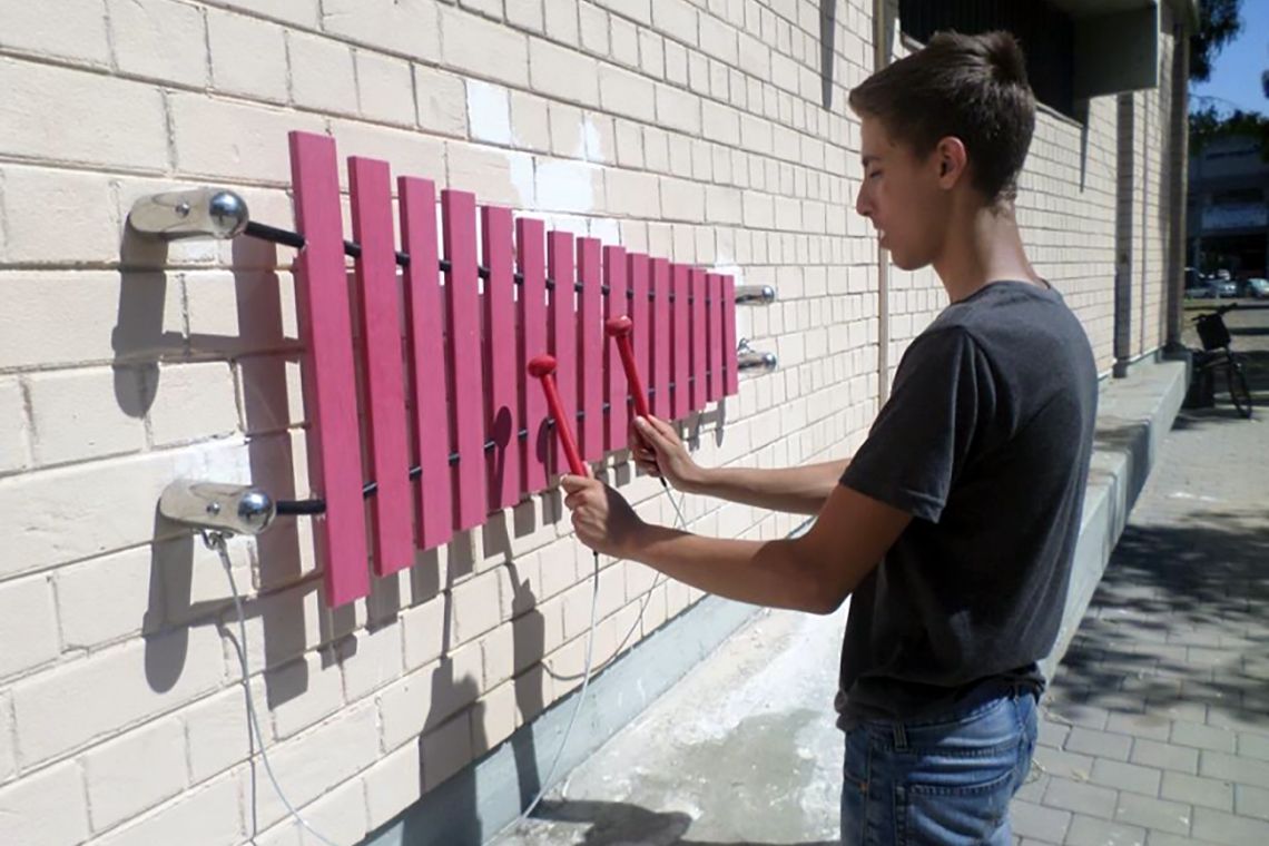 teenage boy playing a pink marimba mounted on a white wall in tel aviv