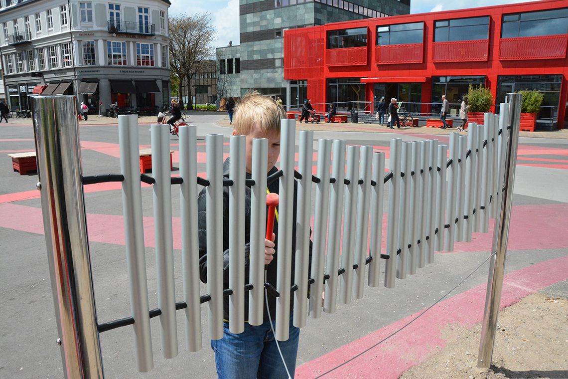 Boy playing a set of musical chimes installed a busy street